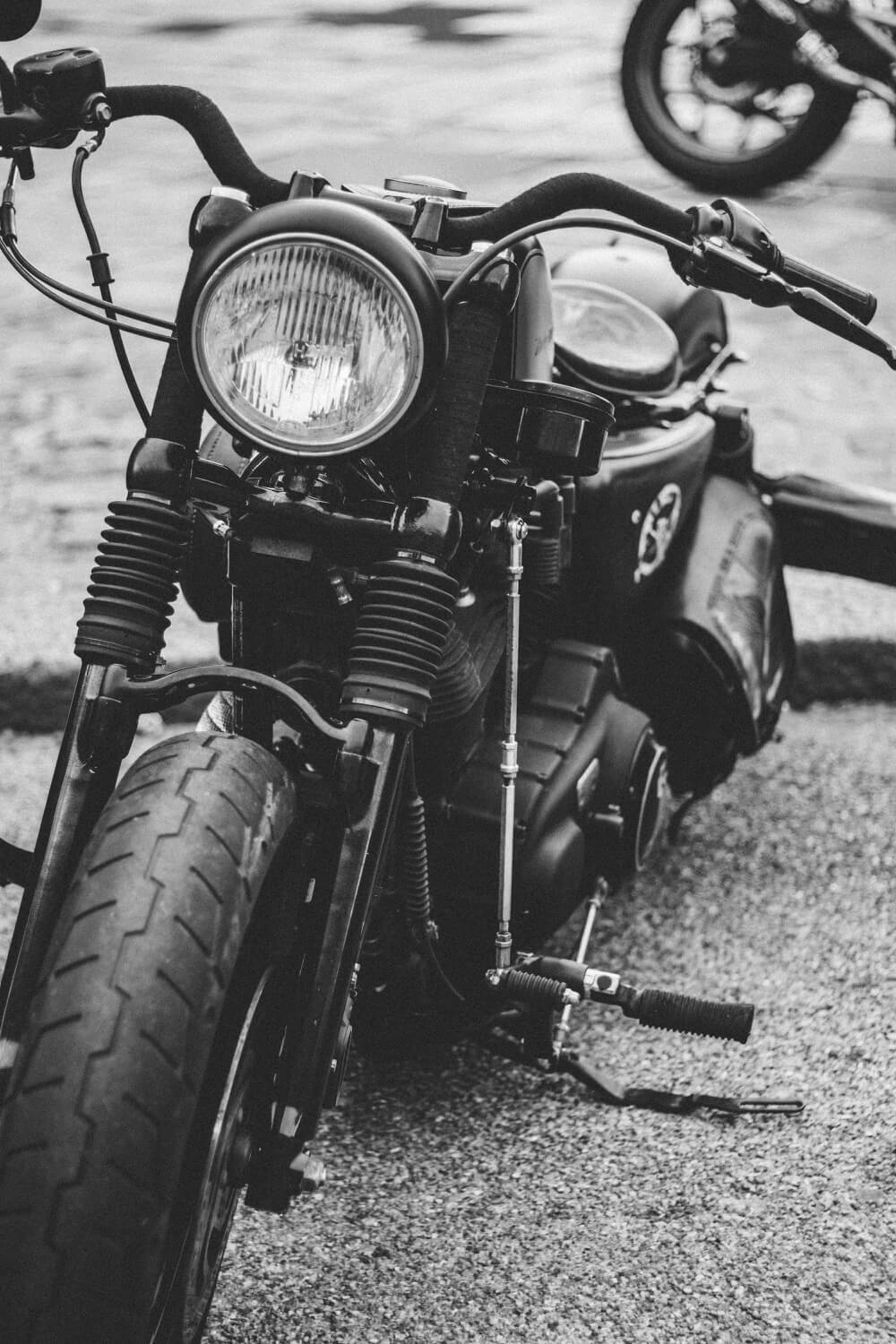 Front view of a vintage motorcycle with a round headlight, visible forks, and a down kickstand on a gravel surface agohorizon.