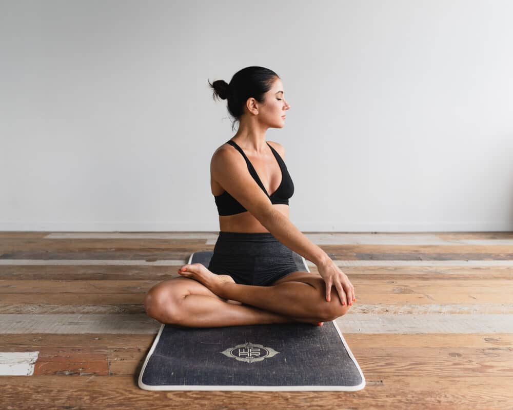dane-wetton-t1NEMSm1rgI-unsplash | Peru Travel Blog Woman sits cross-legged on a yoga mat in a calm room, hands resting on knees in a meditative pose, facing left.