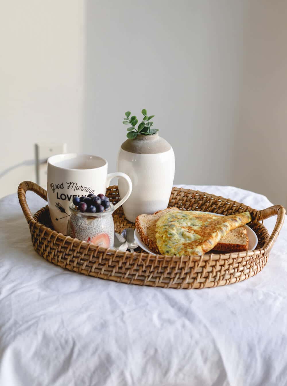shashi-chaturvedula-sHu3yTbaJvU-unsplash | Peru Travel Blog Cozy breakfast tray on a white table: mug with 'Good Morning' text, jar of blueberries, small plant in a vase, and cheese-topped toast on a plate