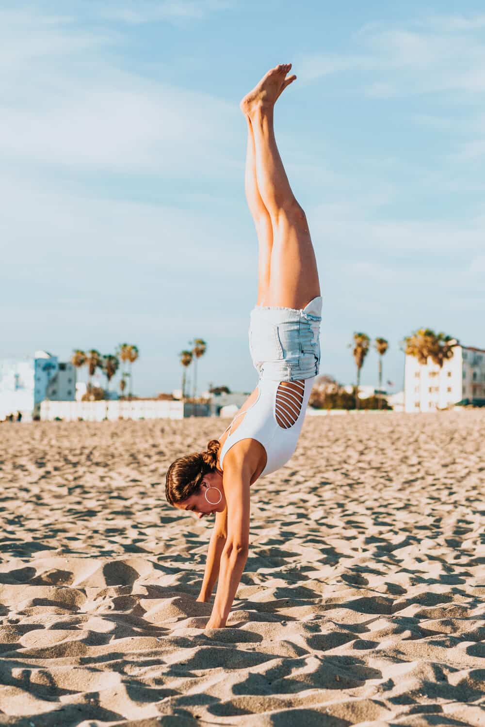 tyler-nix-6Ysa0KzwYmo-unsplash | Peru Travel Blog Woman performing a handstand on a sandy beach, wearing a white swimsuit and light denim shorts, with palm trees in the background.