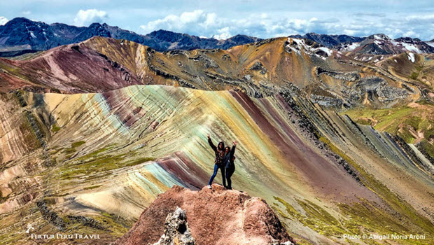 A couple pose on a ridge with Palcoyo 'Rainbow Mountain' in the background