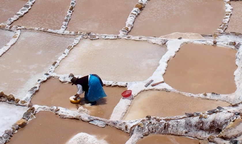 Maras woman harvests salt at the Salineras de Maras (Maras Salt Mines) in Cusco Peru