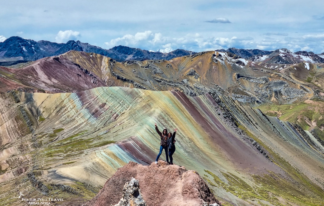 A couple pose on a ridge with Palcoyo 'Rainbow Mountain' in the background