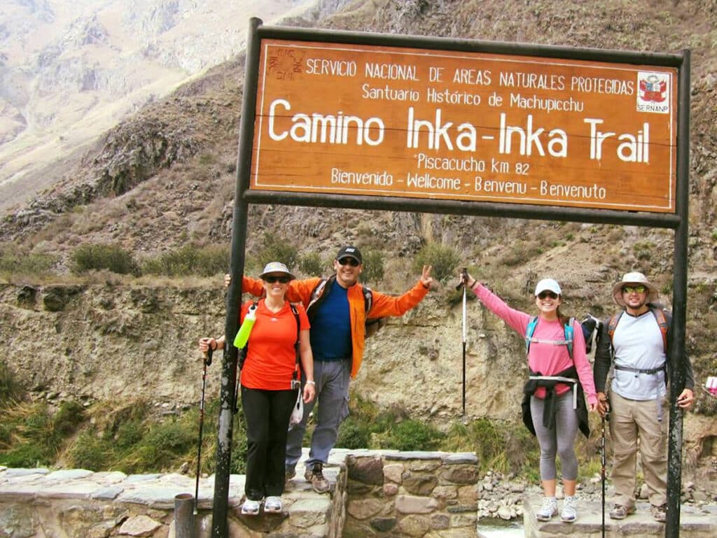 Inca Trail Trailhead at Km 82 — Starting the Classic Hike to Machu Picchu, Peru | Peru Travel Blog Four excited hikers posing under the official Camino Inka — Inca Trail sign at the Piscacucho trailhead (Km 82) within the Machu Picchu Historical Sanctuary, marking the start of the classic 4-day Inca Trail trek to Machu Picchu, Cusco, Peru.