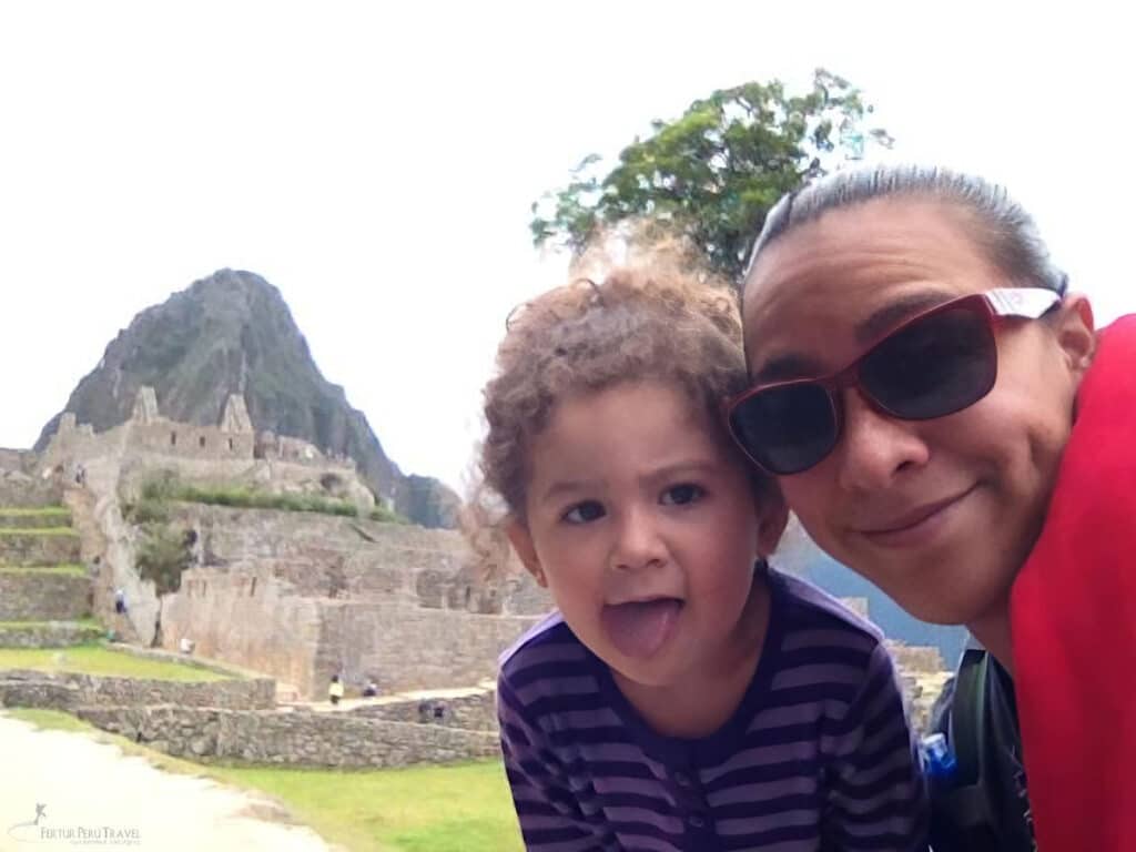 Selfie with a Toddler at Machu Picchu — Visiting Peru with Very Young Children | Peru Travel Blog A playful selfie of a grandmother and a curly-haired toddler making a funny face together inside the Machu Picchu citadel, with the Inca stone terraces and the peak of Huayna Picchu visible in the background, Cusco, Peru. Photo: Fertur Peru Travel.
