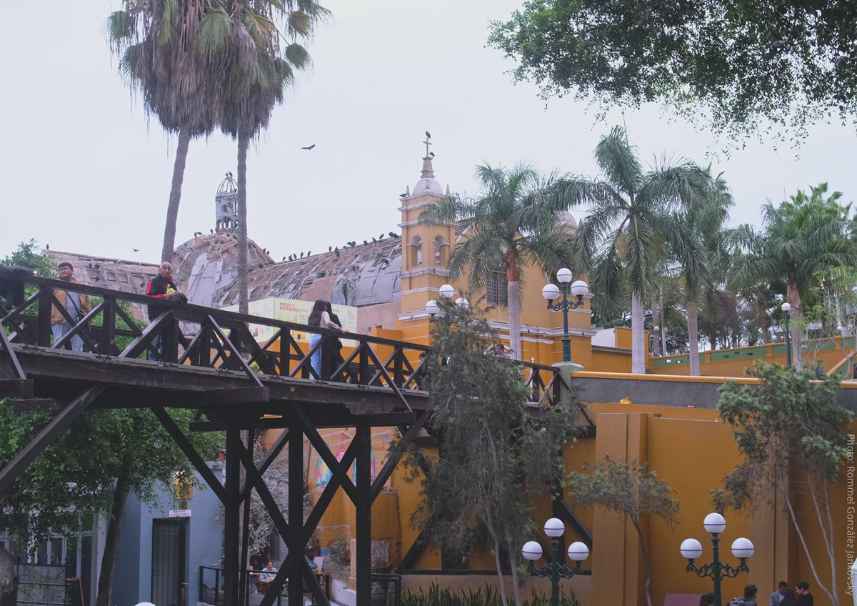 Puente de los Suspiros Footbridge and La Ermita Church Under Restoration, Barranco | Lima, Peru | Peru Travel Blog The historic wooden Puente de los Suspiros footbridge in the foreground with the yellow colonial façade and damaged dome of La Ermita church visible behind palm trees in the bohemian Barranco district of Lima, Peru. Photo: Rommel Gonzalez Jankovsky.