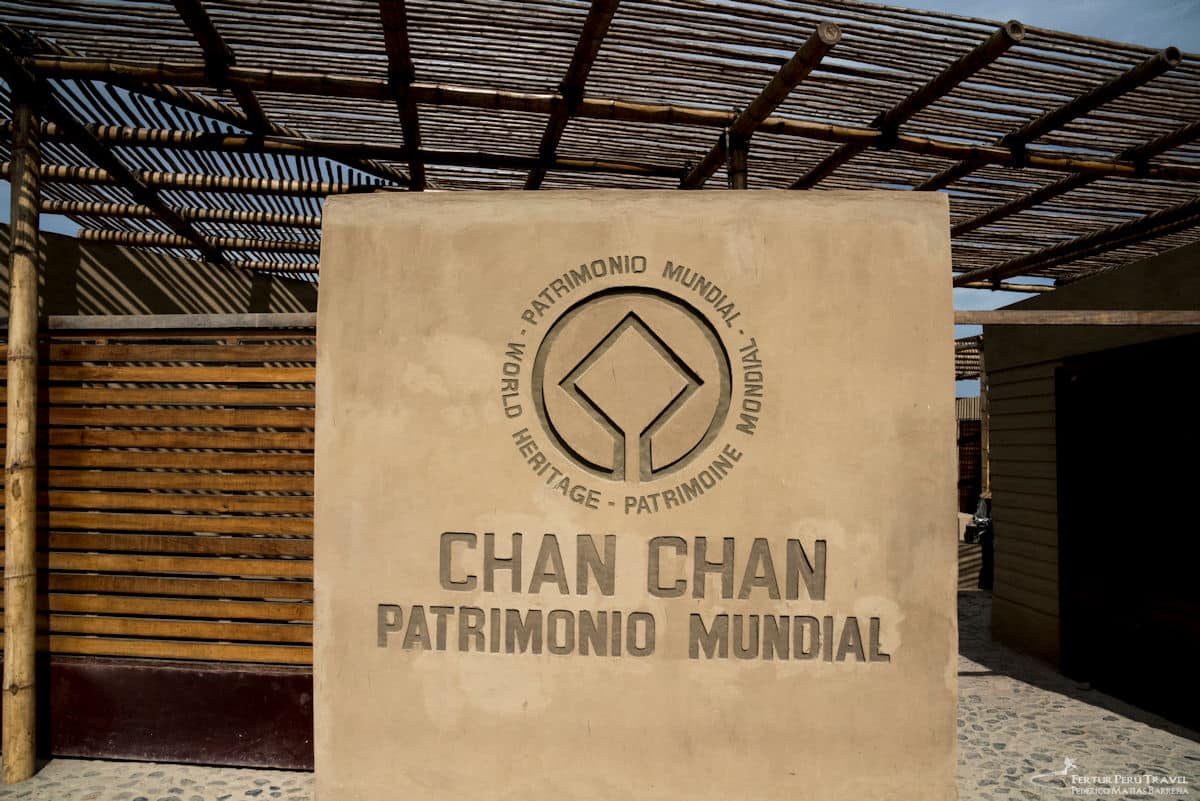 Chan Chan UNESCO World Heritage Site Entrance | Trujillo, Peru | Peru Travel Blog The official entrance sign of Chan Chan archaeological site, bearing the UNESCO World Heritage emblem and the inscription "Chan Chan Patrimonio Mundial" in raised adobe lettering, framed by bamboo columns and a cane roof at the site entrance, Trujillo, La Libertad, Peru. Photo: Fertur Peru Travel / Federico Matías Barreña.