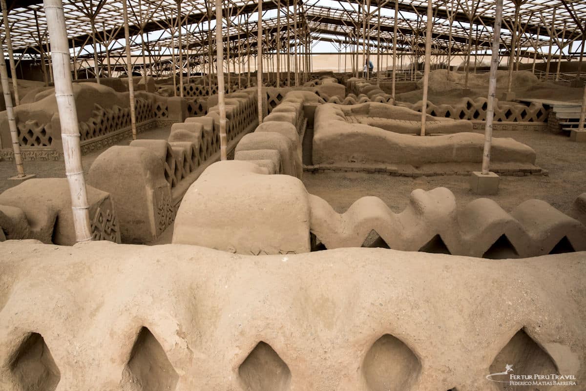 Chan Chan Adobe Friezes Under Protective Cover | Chimú Archaeological Conservation | Trujillo Peru | Peru Travel Blog Interior view of a large metal and bamboo protective roof structure covering the elaborately decorated adobe walls and friezes of the Chan Chan archaeological site, showing wave, diamond, and geometric Chimú relief patterns on the eroded adobe surfaces stretching into the distance, Trujillo, Peru. Photo: Fertur Peru Travel / Federico Matías Barreña.
