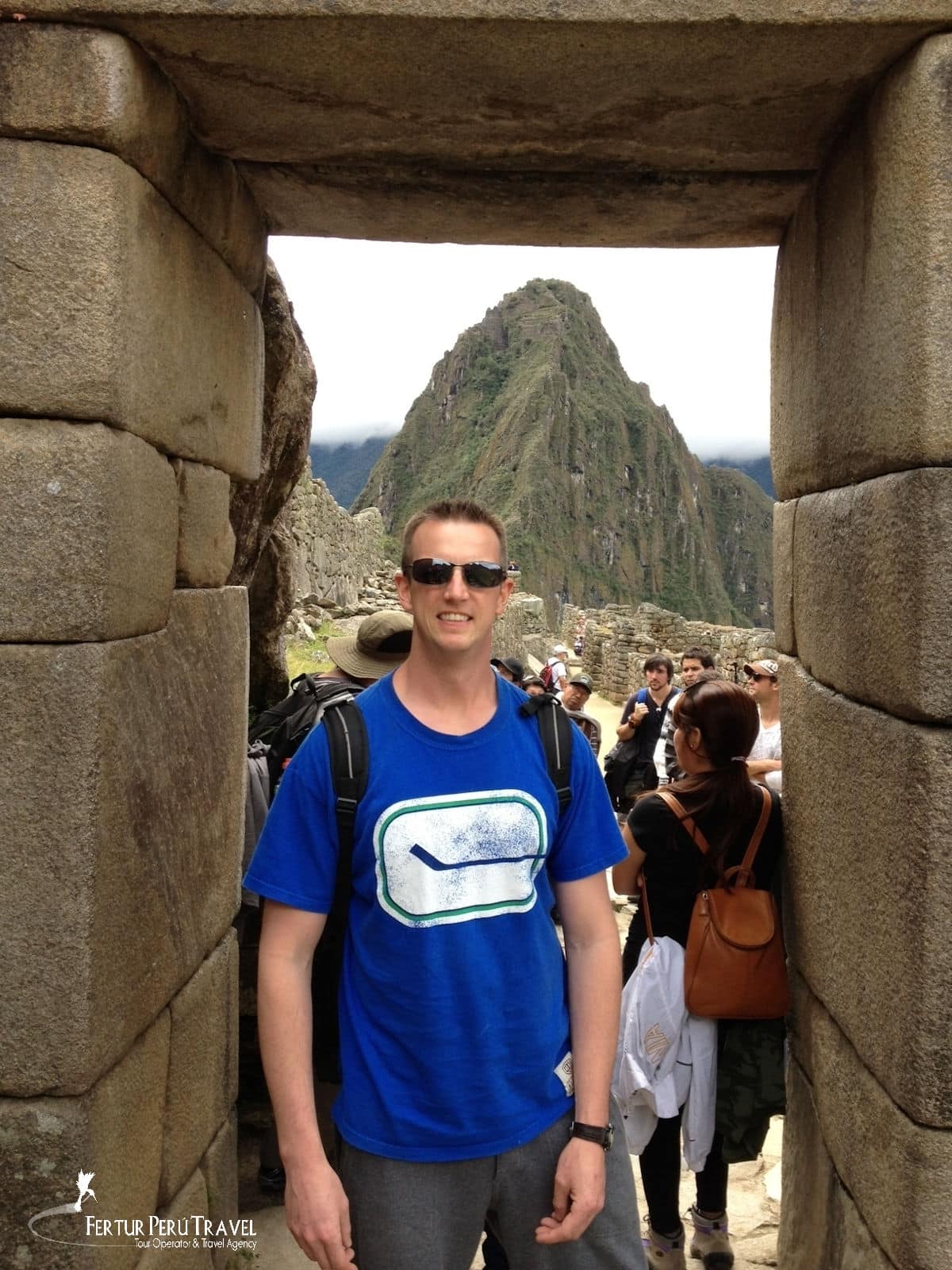 Doorway with Huayna Picchu Mountain Behind, Machu Picchu, Peruu Picchu | Peru Travel Blog A Fertur Peru Travel client poses in one of Machu Picchu's signature trapezoidal Inca stone doorways, with the dramatic peak of Huayna Picchu (2,693 m) rising dramatically through low cloud in the background — one of the most iconic vantage points at the ancient citadel.