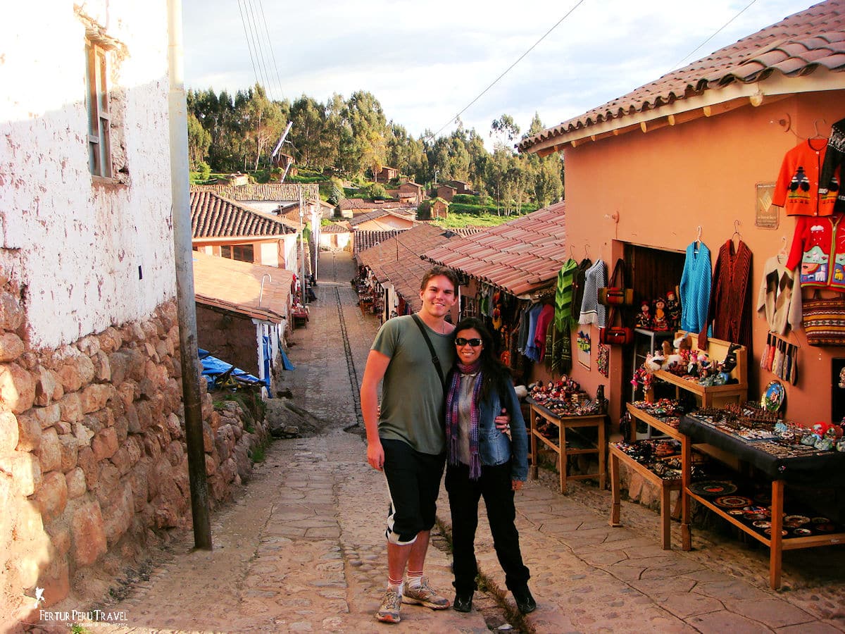 Couple Posing on a Cobblestone Street Lined with Artisan Shops in the Sacred Valley, Cusco, Peru | Peru Travel Blog A smiling couple poses on a narrow cobblestone street flanked by artisan craft stalls selling textiles, ceramics, and souvenirs in a traditional village in the Sacred Valley, Cusco, Peru