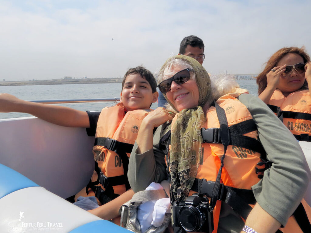 Grandmother and Grandson on a Ballestas Islands Boat Tour, Paracas, Perurandchildren | Peru Travel Blog A smiling grandmother and her young grandson wearing orange life jackets ride a speedboat on a Ballestas Islands wildlife tour off the coast of Paracas, Peru, with the Pacific Ocean and coastline visible behind them