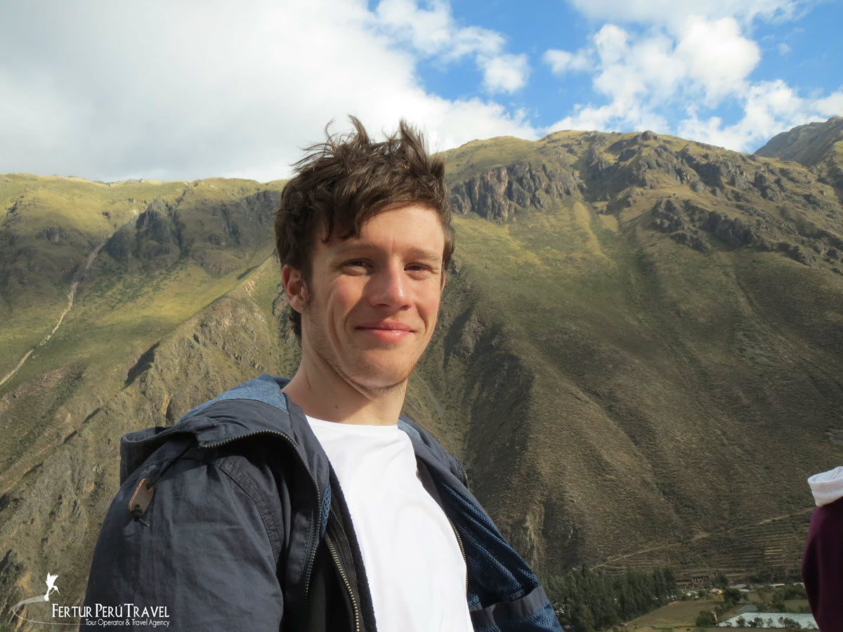 Happy Traveler at a Scenic Overlook in the Sacred Valley of the Incas, Cusco, Peru | Peru Travel Blog A Fertur Peru Travel client enjoys a panoramic viewpoint above the Sacred Valley of the Incas, with the valley's terraced green slopes and rugged Andean ridgeline filling the background.