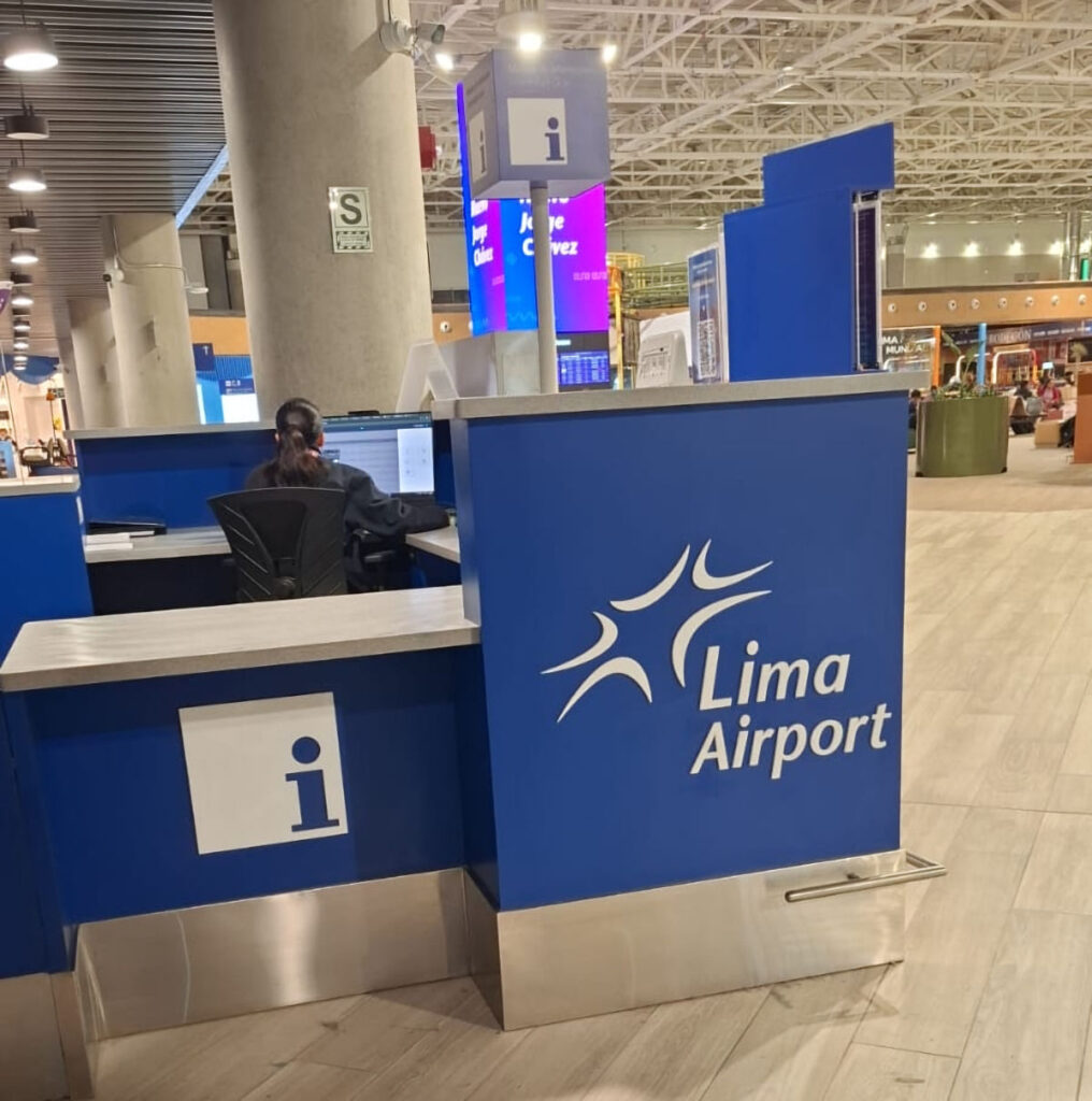 Passenger Information Desk at Jorge Chávez International Airport, Lima, Peru | Peru Travel Blog A staffed passenger information desk with the Lima Airport logo at Jorge Chávez International Airport in Lima, Peru, with the departures hall and flight information screens visible in the background