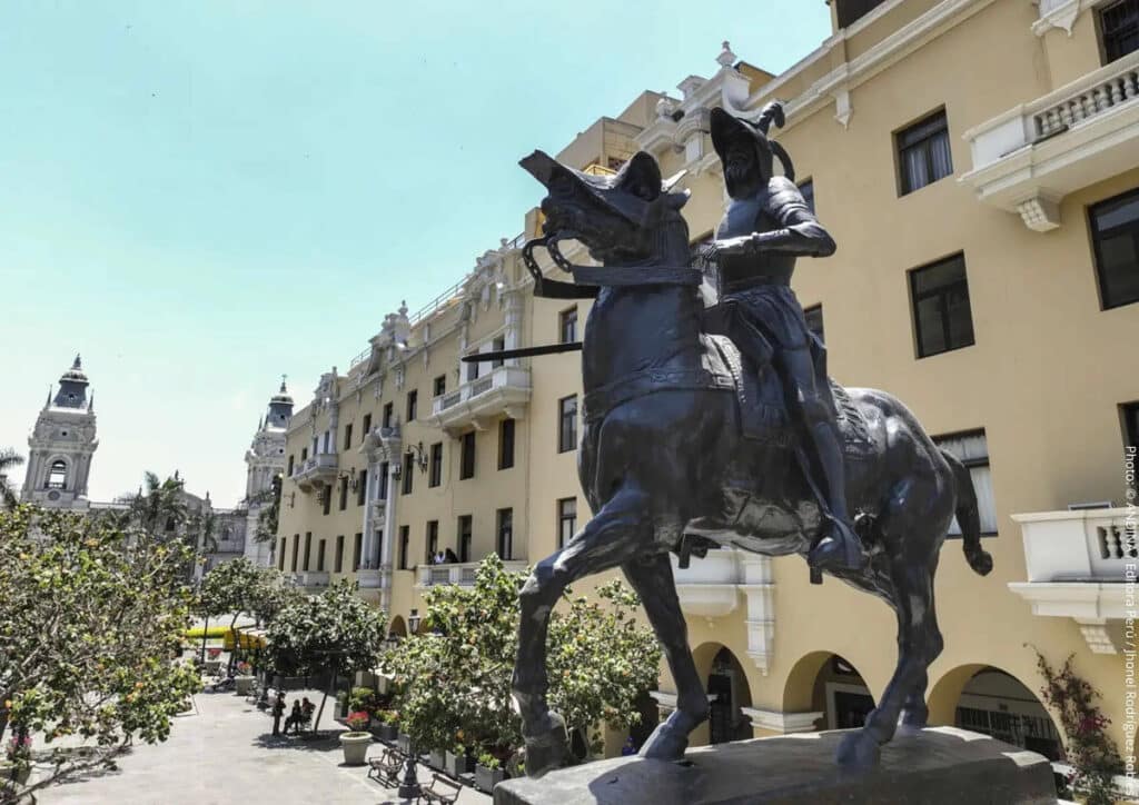 Francisco Pizarro Equestrian Statue, Plaza Mayor, Lima | Photo: ANDINA/Jhonel Rodríguez Robles | Peru Travel Blog A bronze equestrian statue of Spanish conquistador Francisco Pizarro rears dramatically in the foreground of Lima's Plaza Mayor, with the colonial arcades of the Municipal Palace to the right and the Lima Cathedral's towers visible in the background. Photo: © ANDINA / Editora Perú / Jhonel Rodríguez Robles.