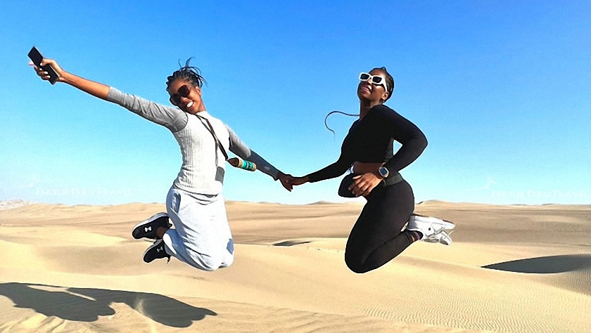Dos clientes de Fertur Perú Travel divirtiéndose en las dunas de arena sobre el Oasis de Huacachina antes de ir a su paseo en buggy.  