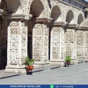 Ornate white sillar stone arches with intricate baroque carvings at the Yanahuara viewpoint in Arequipa, Peru, with potted flowers along the colonnade