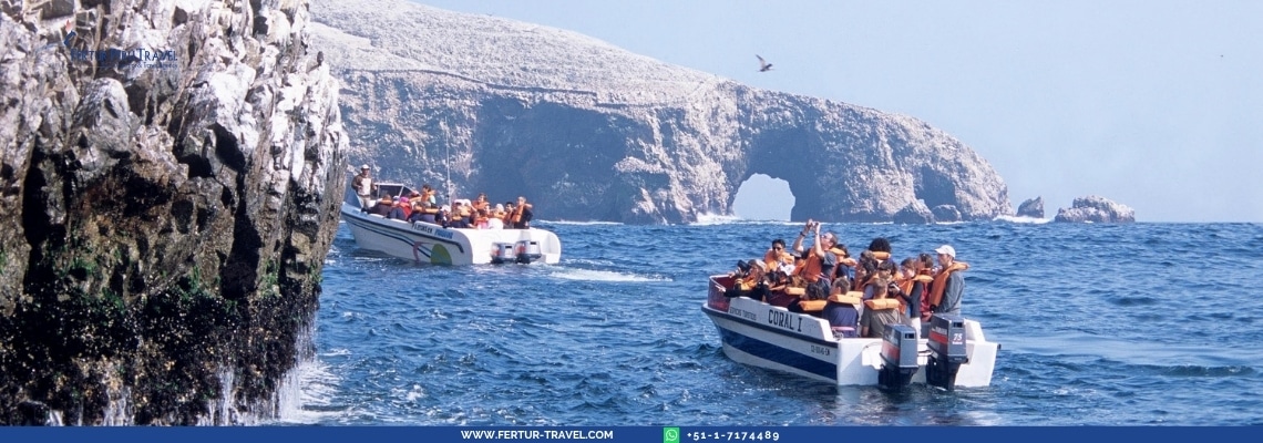 Turistas a bordo de botes con chalecos salvavidas navegando frente a los imponentes acantilados y arcos naturales de las Islas Ballestas en Paracas — el emocionante recorrido en lancha por la fauna marina que usted disfrutará en este tour de 2 días desde Lima.