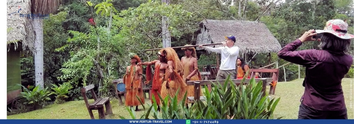 Miembros de una comunidad nativa amazónica en trajes tradicionales de fibras naturales realizando una demostración cultural para viajeros frente a una cabaña con techo de paja del Sinchicuy Lodge en Iquitos — la experiencia de inmersión cultural que usted vivirá en este tour de 3 días por la selva peruana.