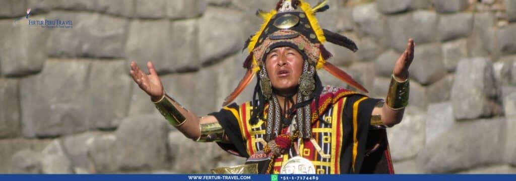 High priest at Inti Raymi festival wearing traditional ceremonial Inca attire with elaborate sun-ray headdress, ornate tunic with geometric patterns in red, yellow and black, golden arm cuffs and large silver earrings, arms raised in ceremonial gesture against the ancient Inca stone walls of Sacsayhuaman fortress