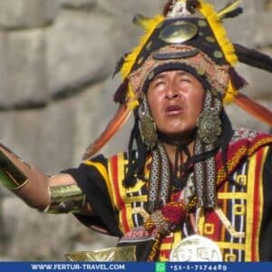 High priest at Inti Raymi festival wearing traditional ceremonial Inca attire with elaborate sun-ray headdress, ornate tunic with geometric patterns in red, yellow and black, golden arm cuffs and large silver earrings, arms raised in ceremonial gesture against the ancient Inca stone walls of Sacsayhuaman fortress