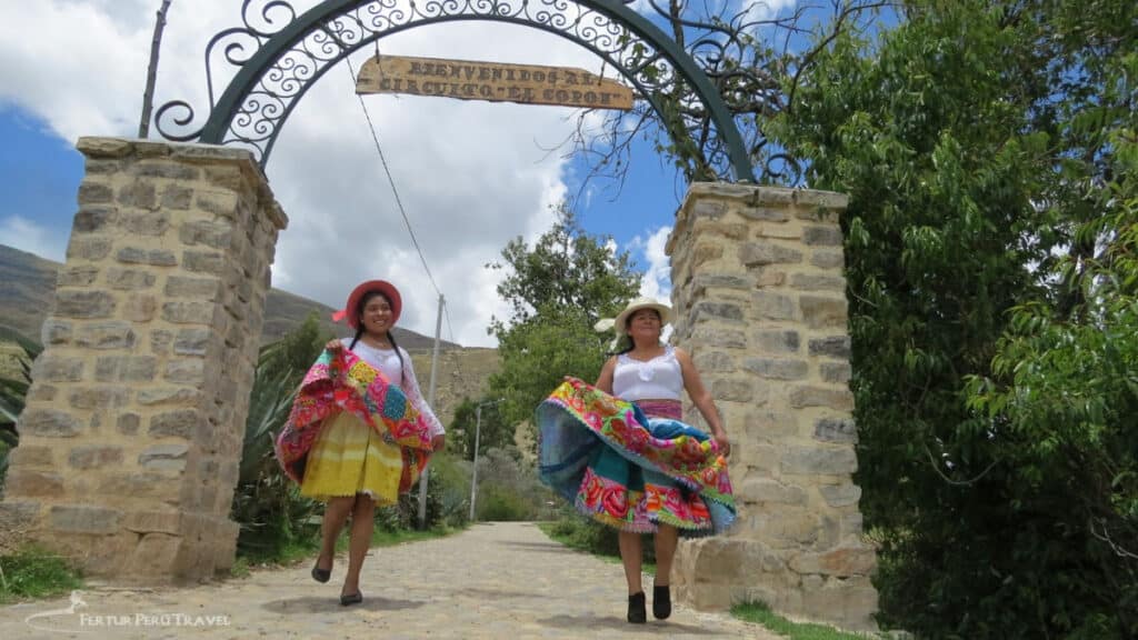 Two women in vibrant traditional dress welcome visitors to Circuito El Copón, a community tourism circuit in the Mantaro Valley near Huancayo, Peru.