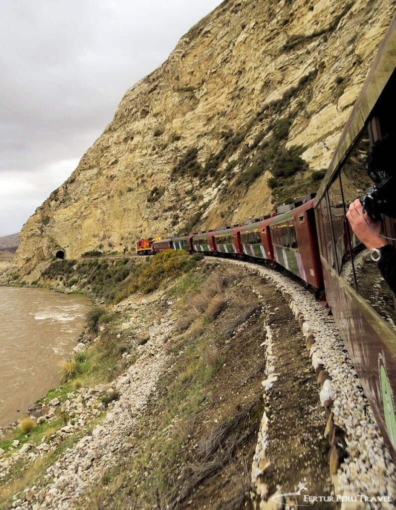 A passenger leans out to photograph the Central Andean Railway as it winds along a cliff above the Rimac River en route to Huancayo, Peru — the world's second-highest railway reaching 15,681 ft. (4,781 m) at Galera Station.