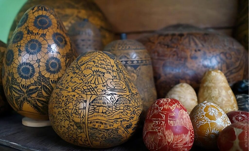 A collection of hand-carved and engraved gourds (mates burilados) of varying sizes, featuring detailed scenes of Andean life, floral patterns, and geometric designs, made in Cochas Chico near Huancayo, Peru.