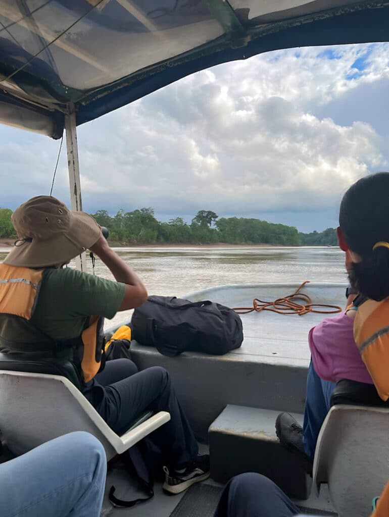 Viajeros con chalecos salvavidas a bordo de un bote motorizado con cubierta en el río Tambopata, de camino a un ecolodge, Perú.